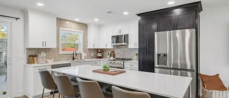 Una cocina moderna con armarios blancos, un refrigerador de acero inoxidable y una isla central con taburetes de bar.