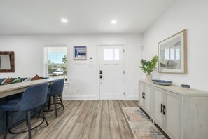 A modern kitchen with a dining area, wooden flooring, and a white door. - Armistead Abode - Walk to TAMU & Kyle Field! (College Station)