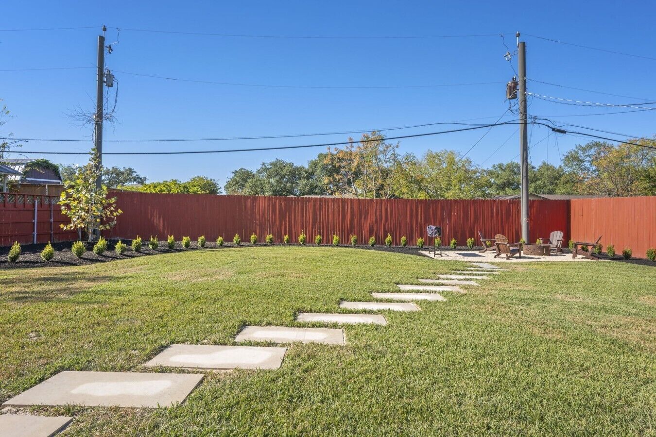 A backyard with a red fence, a paved pathway, and outdoor furniture.