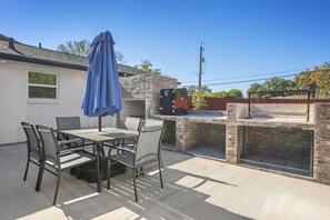 An outdoor patio with a table and chairs, a blue umbrella, and a brick barbecue area. - Armistead Abode - Walk to TAMU & Kyle Field! (College Station)