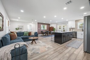 A modern kitchen with a central island, a dining area with chairs, and a living room with a sofa and coffee table. - Armistead Abode - Walk to TAMU & Kyle Field! (College Station)