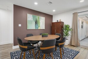 A conference room with a round table, six chairs, a cabinet, and a large abstract painting on the wall. - Armistead Abode - Walk to TAMU & Kyle Field! (College Station)