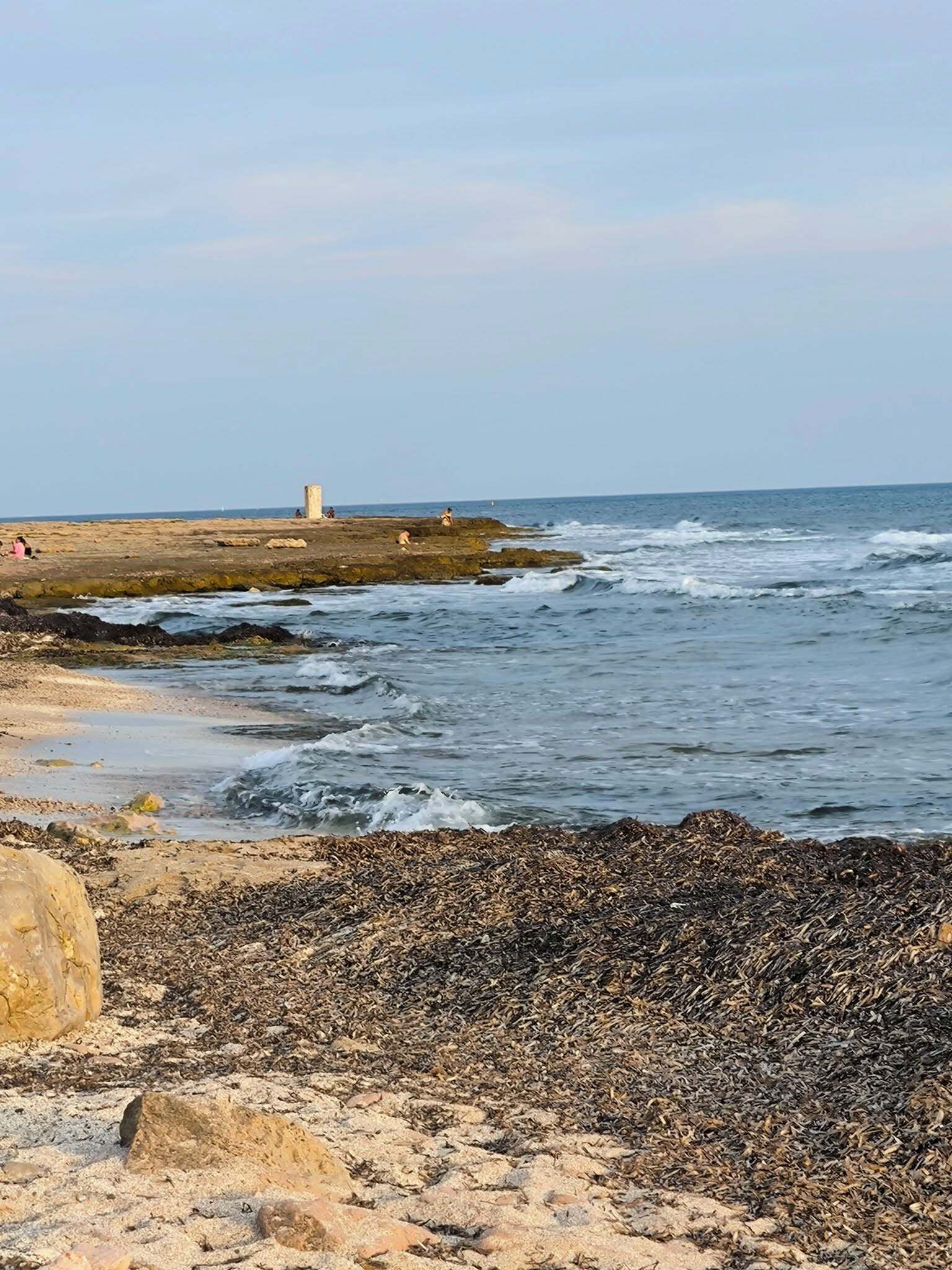 Uma praia rochosa com ondas, um farol e um céu claro.