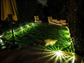 A well-lit outdoor area with a lawn, seating, and potted plants.