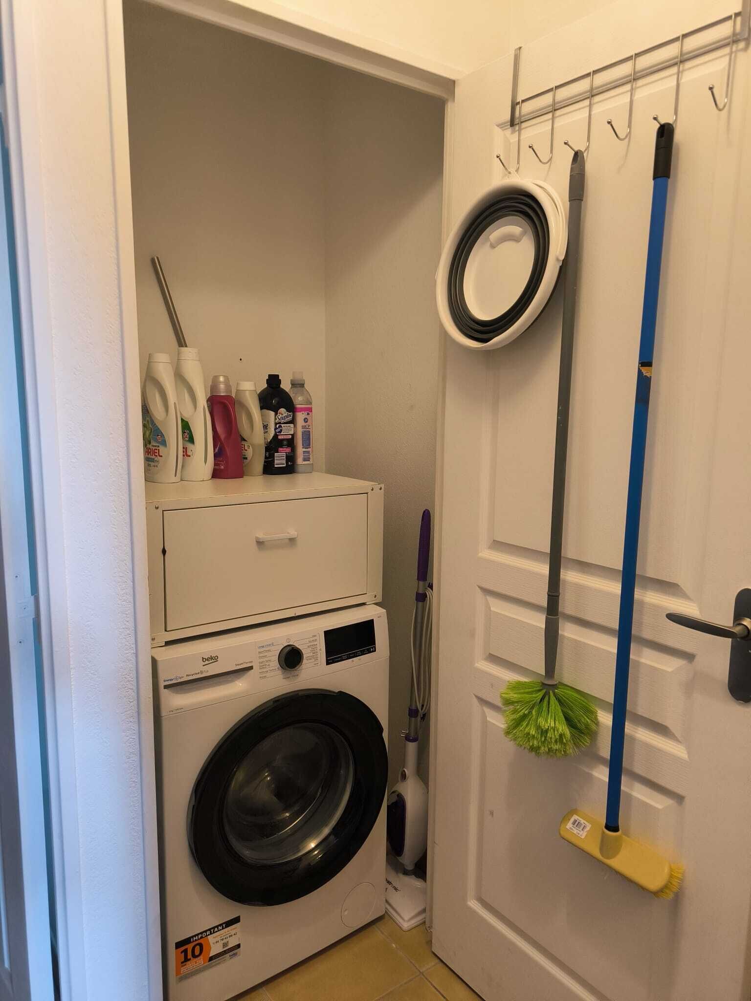 A laundry area with a washing machine, a mop, and cleaning supplies.