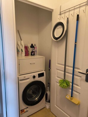Un espace dédié à la lessive, comprenant un lave-linge, une serpillière et des produits de nettoyage.