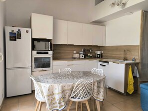 A compact kitchen with a dining area, equipped with a refrigerator, oven, microwave, and coffee maker.