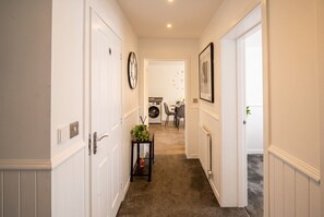 A hallway with a carpeted floor, white walls, and a door leading to a room with a radiator.