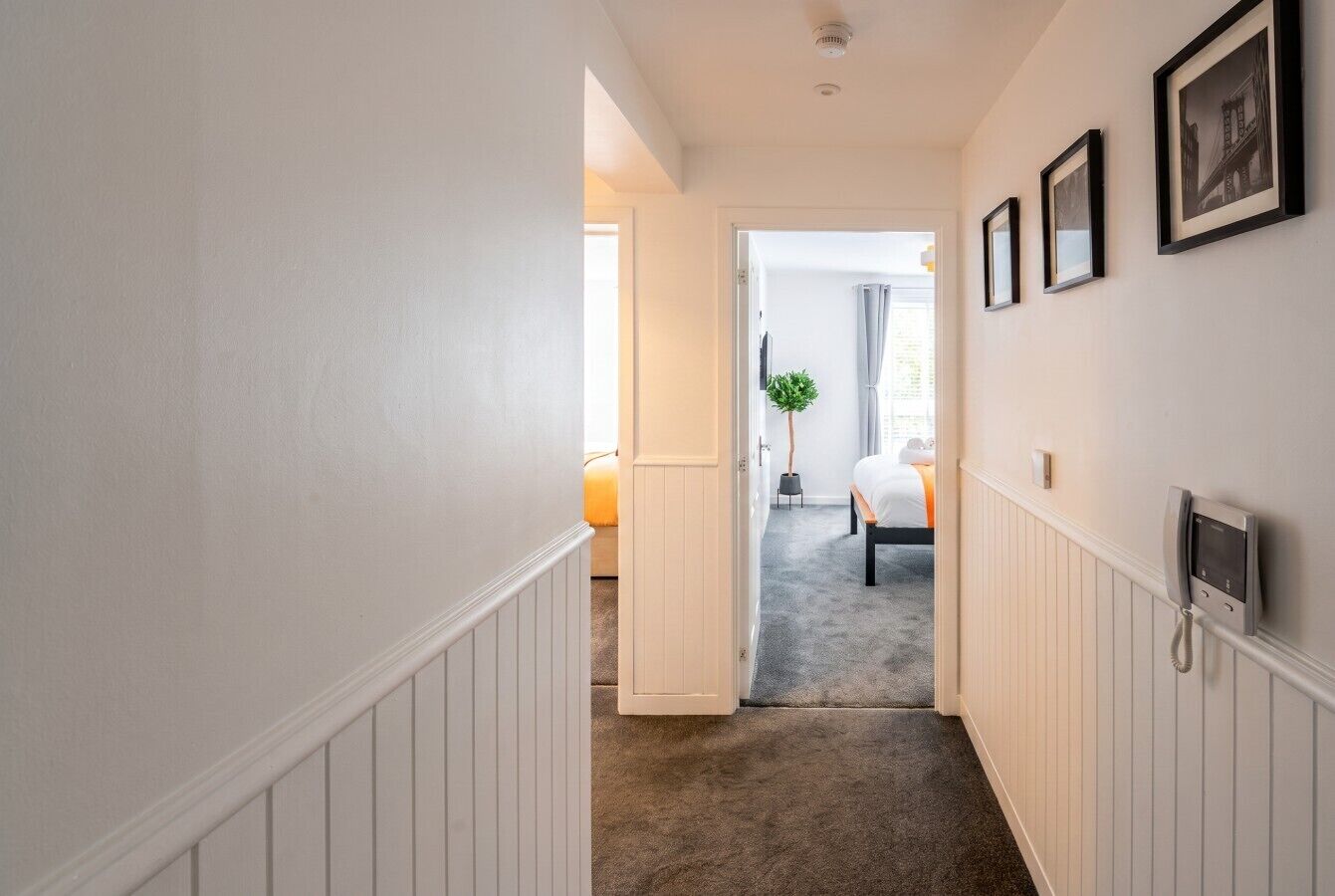 A hotel hallway with a door leading to a bedroom, a telephone on the wall, and a framed picture.