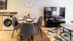 A modern living room with a dining area, a flat-screen TV, a clock, and a washing machine. - 2-Bed Flat Sleeps 4 with Parking · Walk to Historic Dockyard Chatham (Gillingham)
