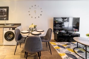 A modern living room with a dining area, a flat-screen TV, a clock, and a washing machine. - 2-Bed Flat Sleeps 4 with Parking · Walk to Historic Dockyard Chatham (Gillingham)