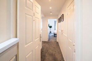 A hallway with white doors, a carpeted floor, and a bed in the distance. - 2-Bed Flat Sleeps 4 with Parking · Walk to Historic Dockyard Chatham (Gillingham)