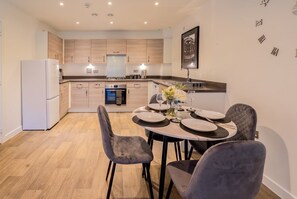 A modern kitchen with wooden cabinets, a built-in oven, and a dining area with a round table and chairs.