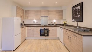 A modern kitchen with built-in appliances, wooden cabinets, and a central island. - 2-Bed Flat Sleeps 4 with Parking · Walk to Historic Dockyard Chatham (Gillingham)