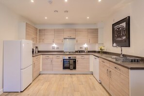 A modern kitchen with built-in appliances, wooden cabinets, and a central island. - 2-Bed Flat Sleeps 4 with Parking · Walk to Historic Dockyard Chatham (Gillingham)