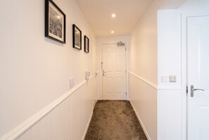 A hallway with white wainscoting, a carpeted floor, and a white door at the end.