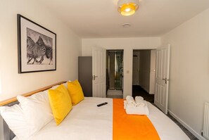 Una camera d'albergo con un letto, un quadro appeso al muro e un bagno visibile attraverso una porta aperta.