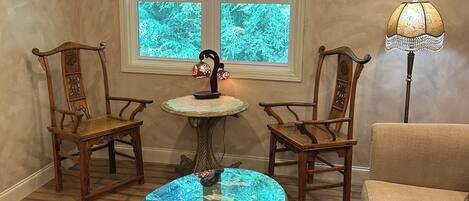 Une pièce avec une table ronde en verre, deux chaises en bois, une lampe et une vue par la fenêtre.