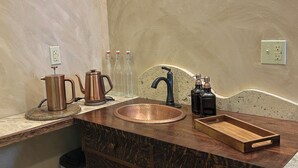A bathroom with a copper sink, wooden vanity, and a towel rack.