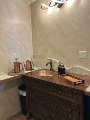 A bathroom with a copper sink, wooden vanity, and a towel rack.
