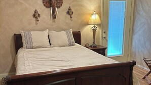 A large bed with a wooden frame, a patterned rug, and a lamp on a bedside table.