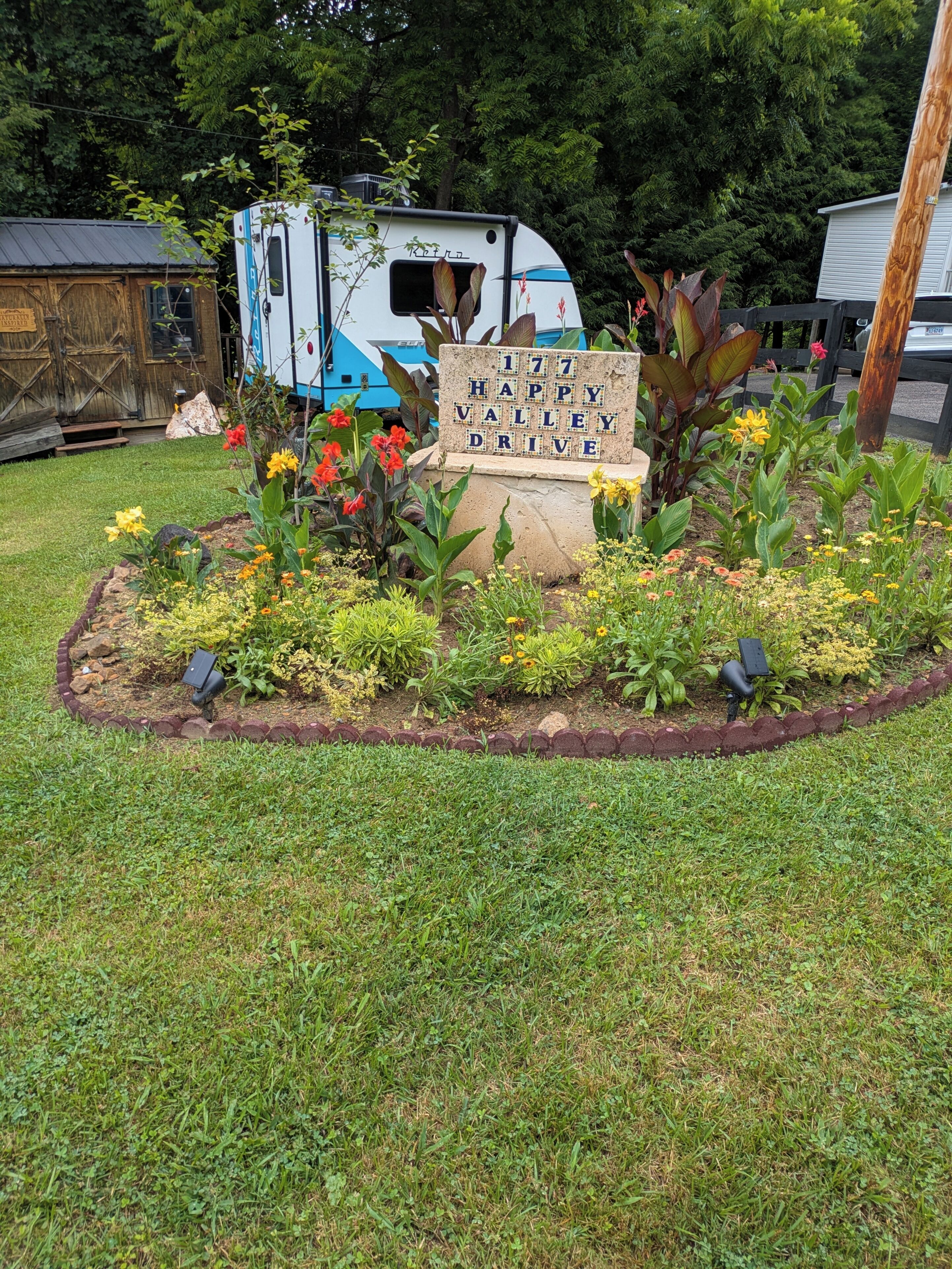 Ein Gartenbereich mit einem Schild, auf dem '177 Happy Valley Drive' steht, umgeben von verschiedenen Pflanzen und Blumen.