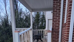 A wooden deck with a railing, a barbecue grill, and a brick building.