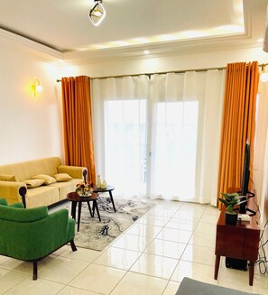 Un salon avec un canapé, un fauteuil vert, une table basse et un téléviseur.