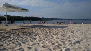 Ein Sandstrand mit Menschen und einem Gewässer im Hintergrund.