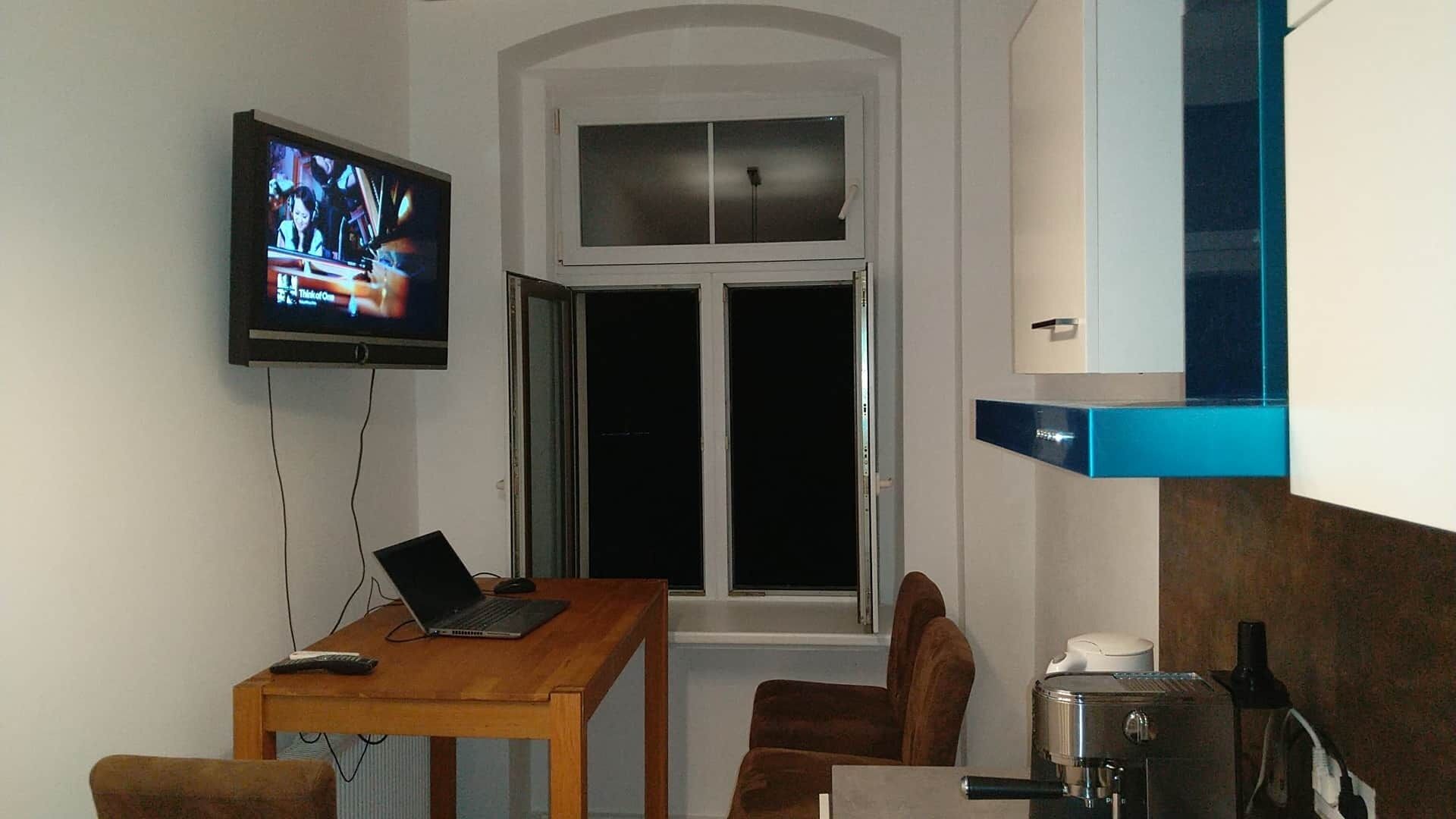 A small room with a television, a laptop on a table, a window, and a coffee machine.
