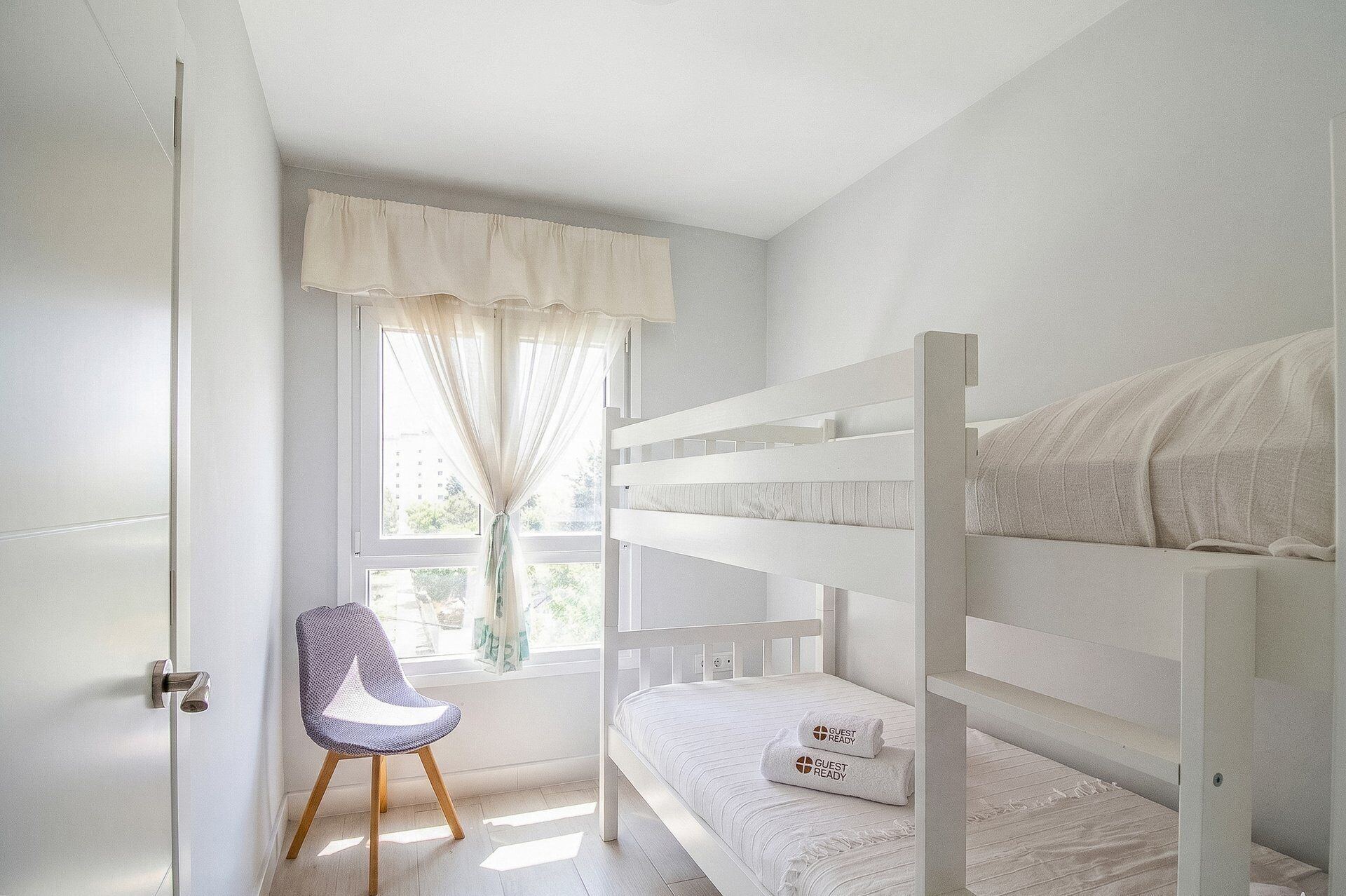 A child's bunk bed with a window, a chair, and a door.