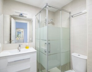 Een moderne badkamer met een glazen douchecabine, een wit wastafelmeubel met een spiegel en een toilet.