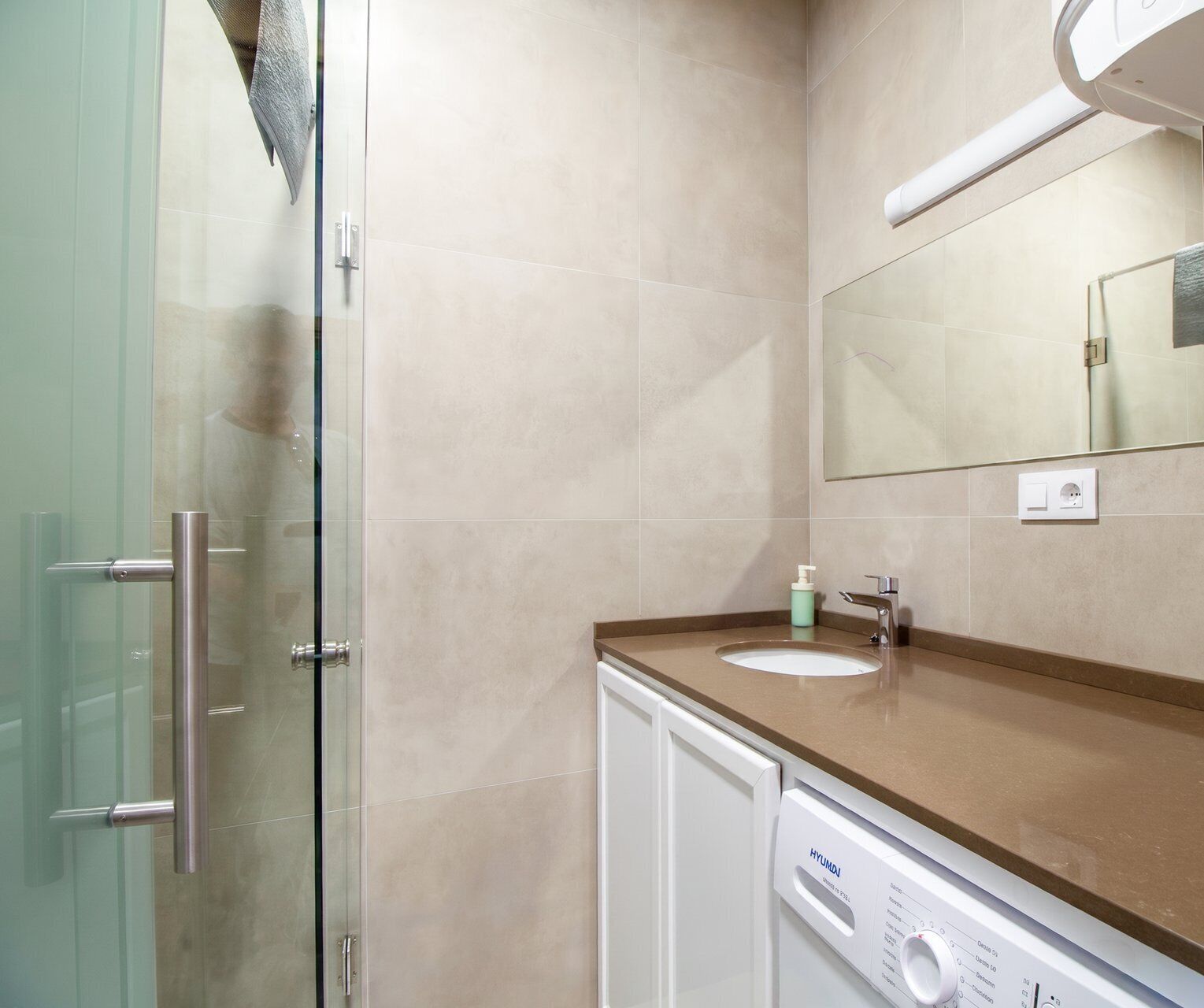A bathroom with a glass shower door, a sink with a mirror above it, and a washing machine.