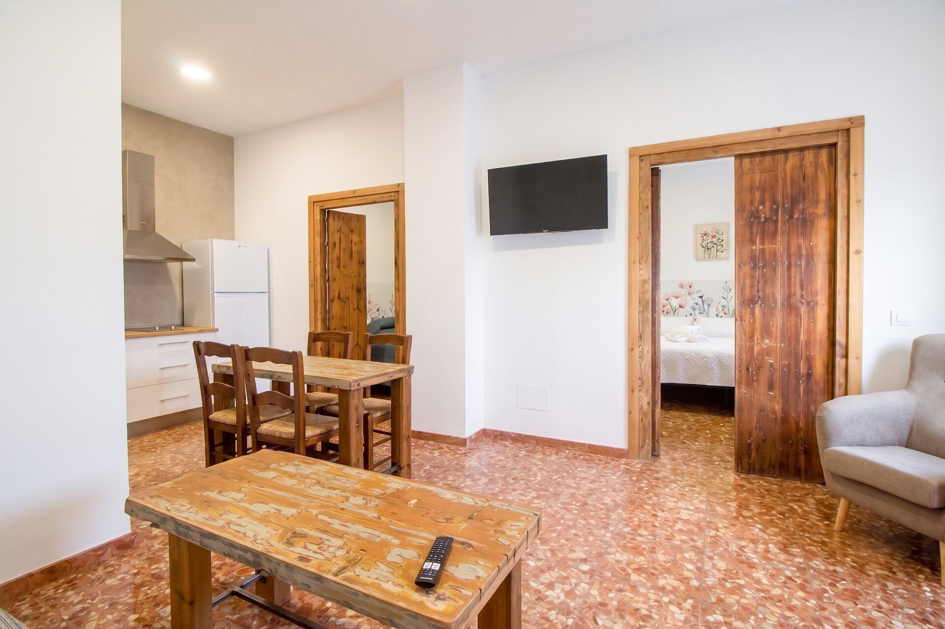 A compact living space with a dining area, kitchenette, and a TV mounted on the wall.