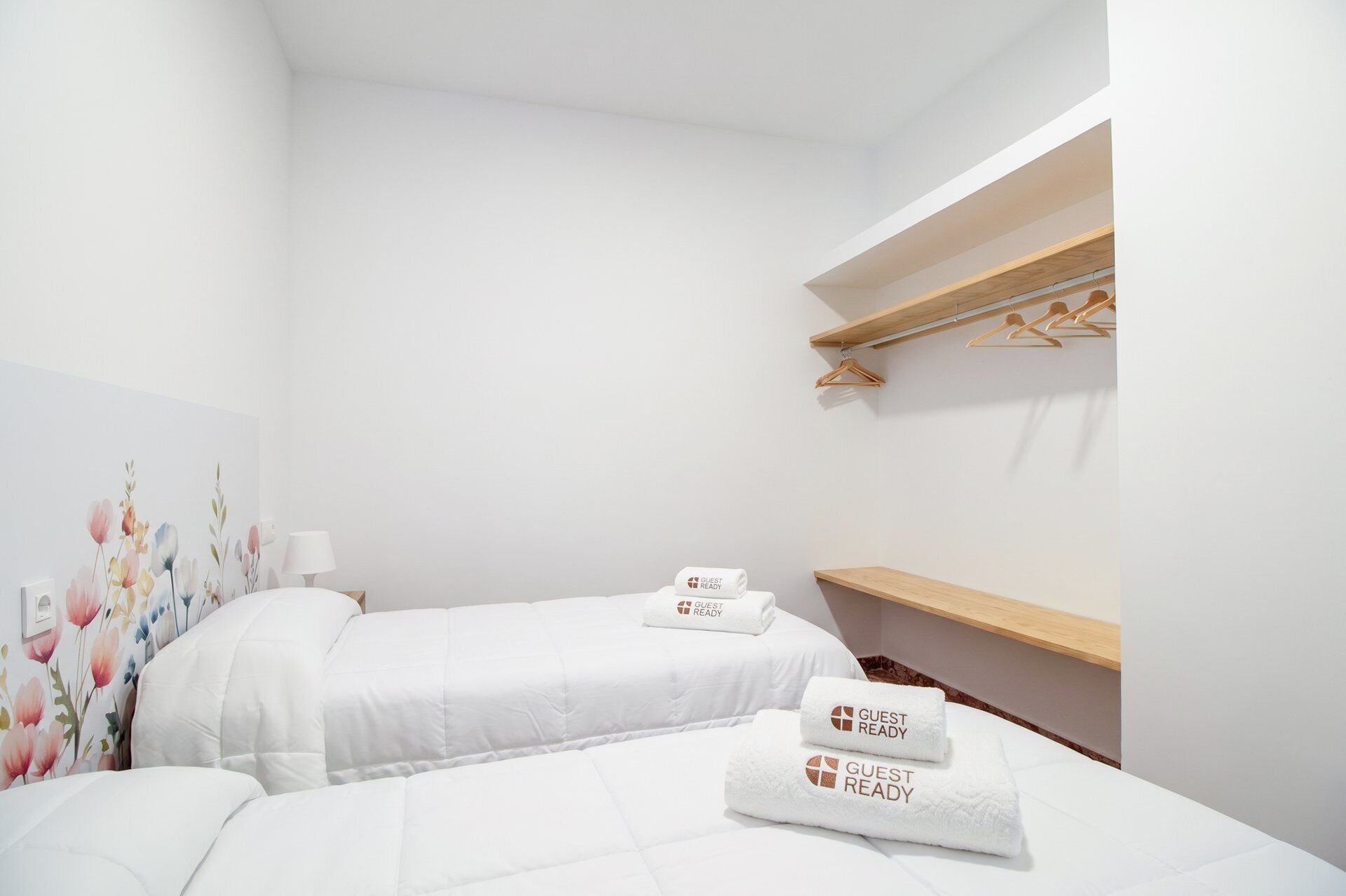 Une chambre d’hôtel avec deux lits, une étagère en bois avec des cintres et une décoration murale à motifs floraux.
