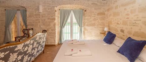 Um quarto com cama, escrivaninha e janela com cortinas.