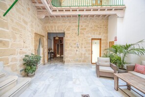 A stone-walled interior with a wooden balcony, a wicker sofa, and a potted plant. - GuestReady - La Cruz 1C (El Puerto de Santa María)