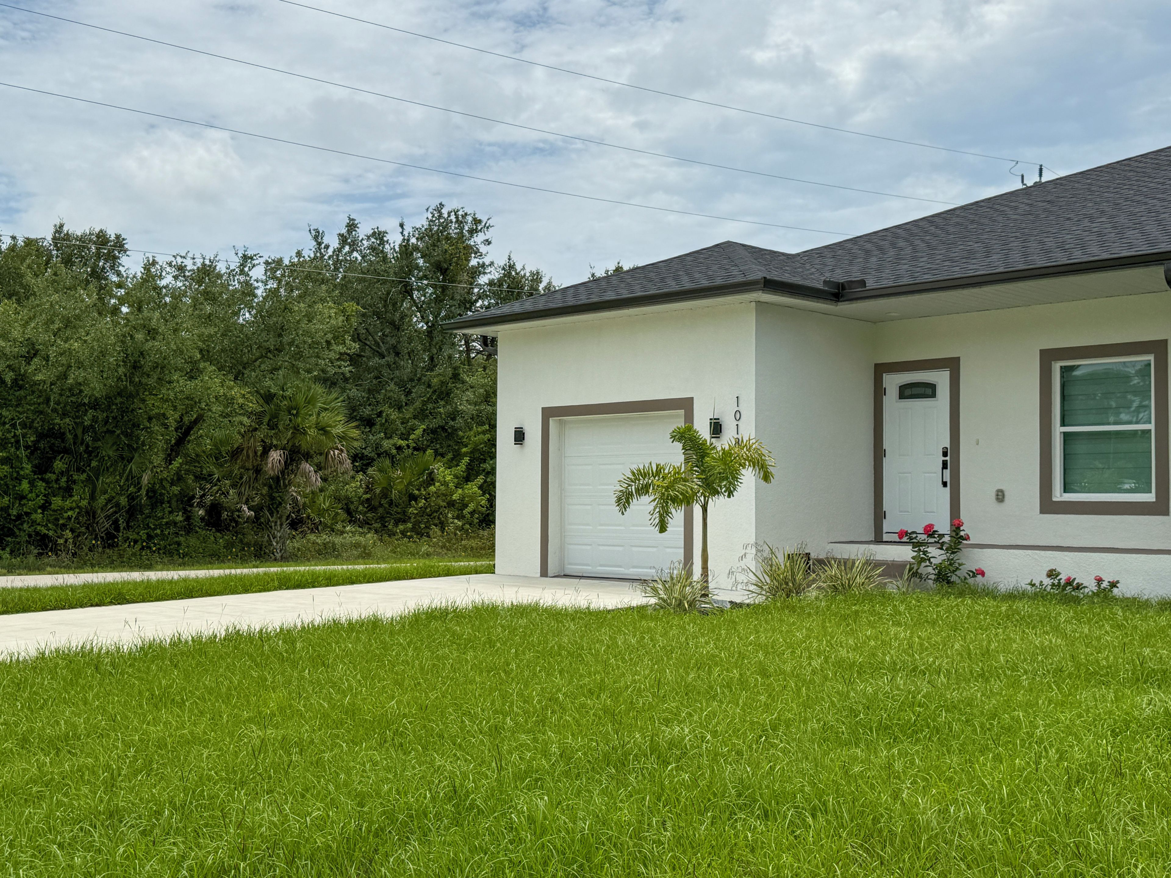 Una casa de un piso con fachada blanca, puerta de garaje y un pequeño jardín frontal con césped y una palmera.