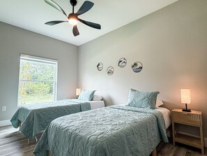Un dormitorio con dos camas, ventilador de techo, ventana con vistas y decoración en la pared.