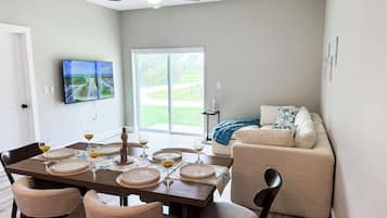Un comedor con una mesa preparada para cuatro personas, un sofá y un televisor montado en la pared.