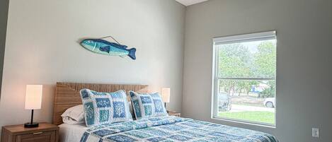 Un dormitorio con cama, mesitas de noche, ventilador de techo, ventana y un adorno de pez montado en la pared.