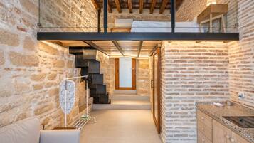 A modern interior with exposed brick walls, a staircase leading to a loft, and a kitchen area with a countertop and cabinets.