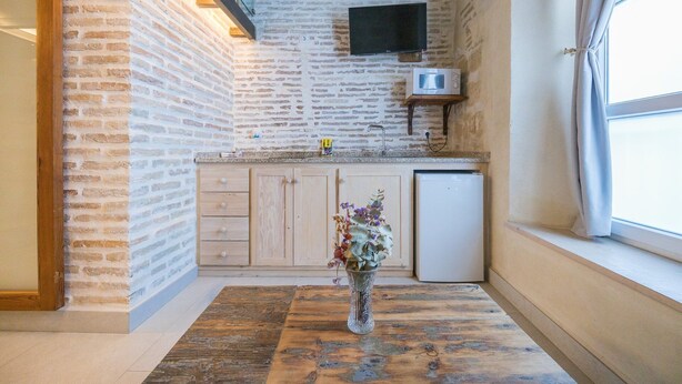 A kitchen with a brick wall, wooden cabinets, a white refrigerator, and a vase with flowers on the floor. - GuestReady - La Cruz Bajo C (El Puerto de Santa María)
