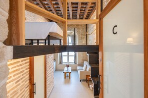 A loft-style room with exposed wooden beams, a stone wall, and a white ceiling. - GuestReady - La Cruz Bajo C (El Puerto de Santa María)