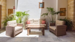 A sunlit patio area with wicker furniture, a wooden table, and potted plants. - GuestReady - La Cruz Bajo C (El Puerto de Santa María)