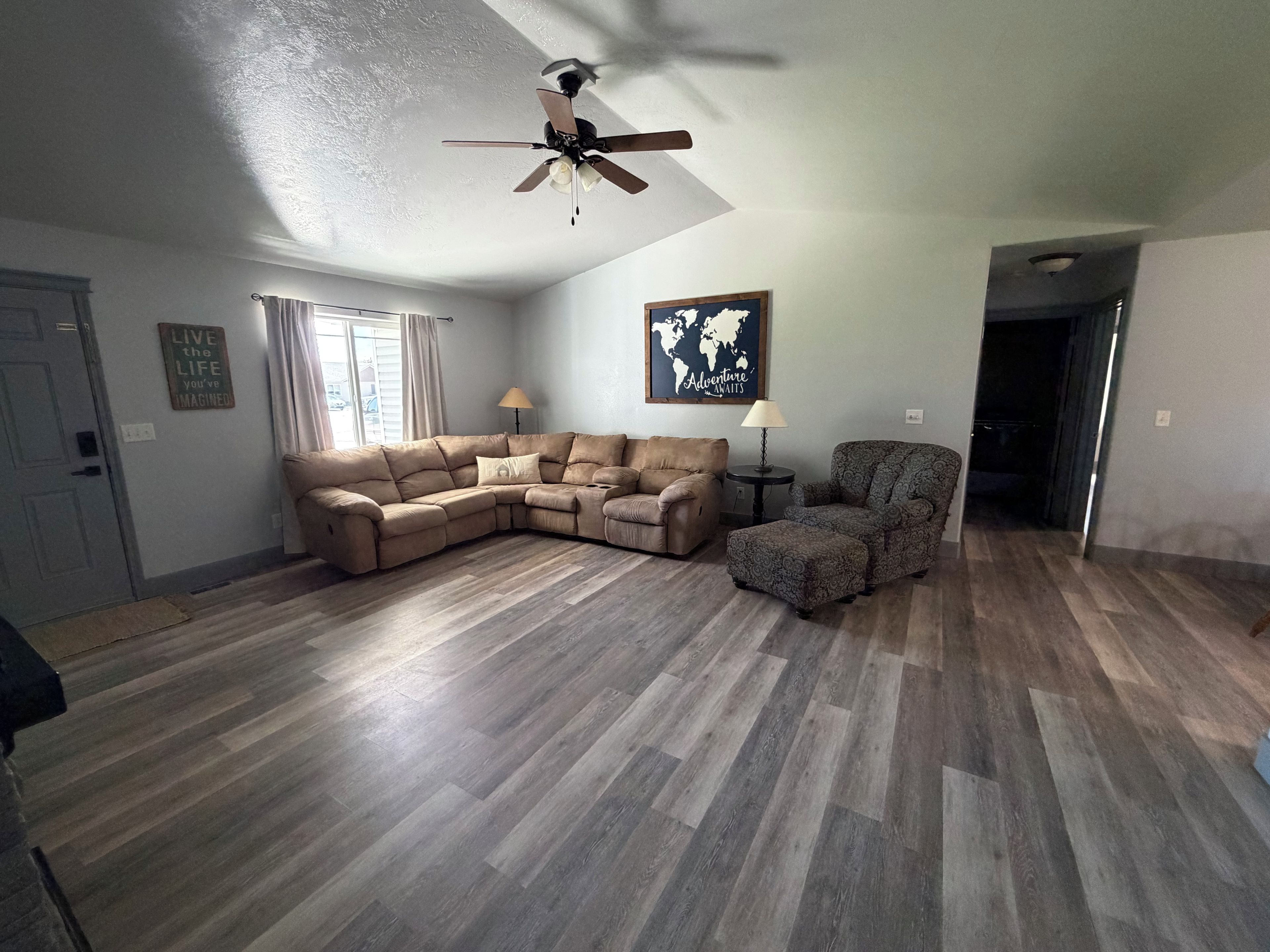 A living room with a sectional sofa, a patterned armchair, a small side table, and a ceiling fan.