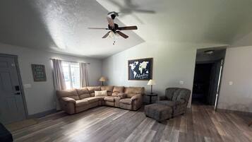 A living room with a sectional sofa, a patterned armchair, a small side table, and a ceiling fan.