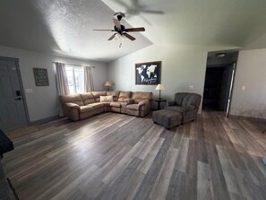 A living room with a sectional sofa, a patterned armchair, a small side table, and a ceiling fan. - Adventure Hub (Filer)