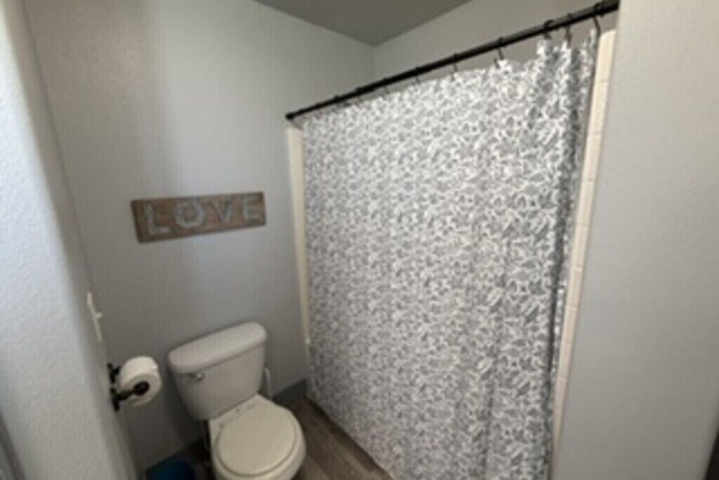 A bathroom with a toilet, a shower curtain, and a wall-mounted sign that says 'LOVE'.