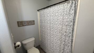 A bathroom with a toilet, a shower curtain, and a wall-mounted sign that says 'LOVE'.